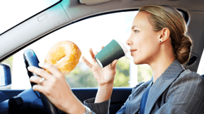 Driver distracted by juggling a phone, food, and a drink while driving.