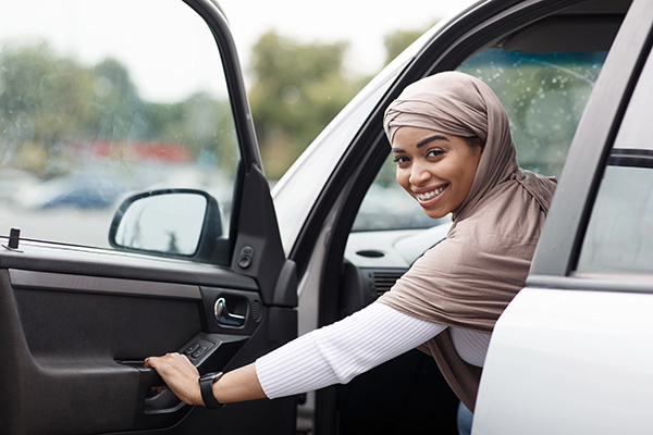 Female driver smiling beside a car, ready for a private driving lesson.