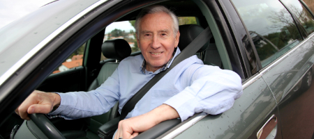 Senior driver smiling behind the wheel after completing a RoadWise defensive driving refresher course.