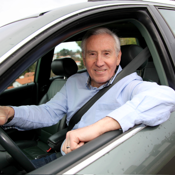 Senior driver smiling behind the wheel after completing a RoadWise defensive driving refresher course.