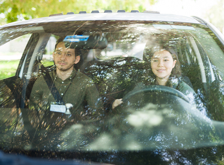 Adult instructor pointing ahead while a teen student practices driving.