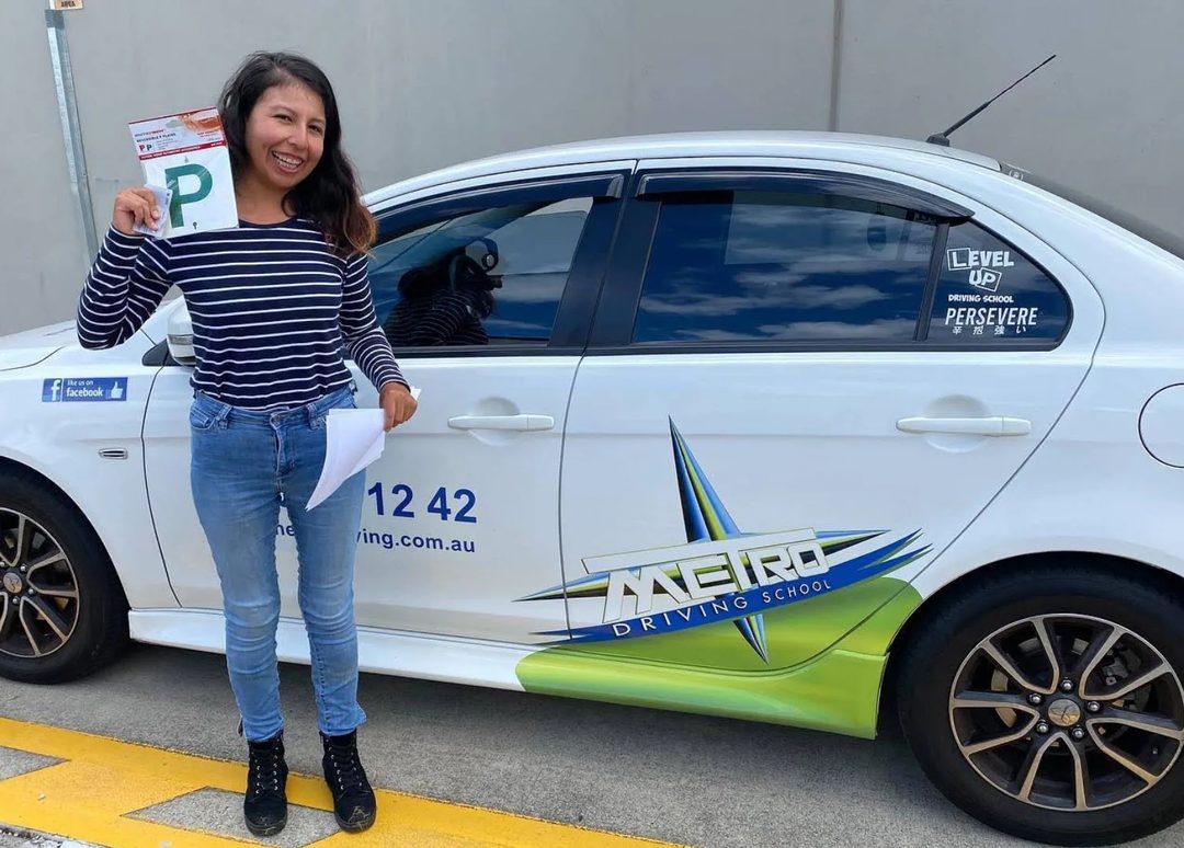 A Metro Driving School learner holding their green P-plates beside a Metro dual-control car after passing the driving test