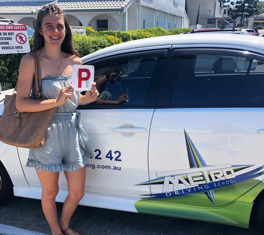 A Metro Driving School learner holding their green P-plates beside a Metro dual-control car after passing the driving test