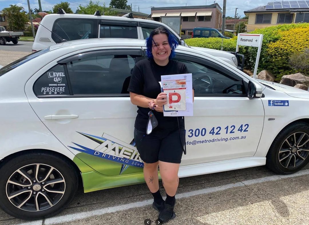 A Metro Driving School learner holding their green P-plates beside a Metro dual-control car after passing the driving test