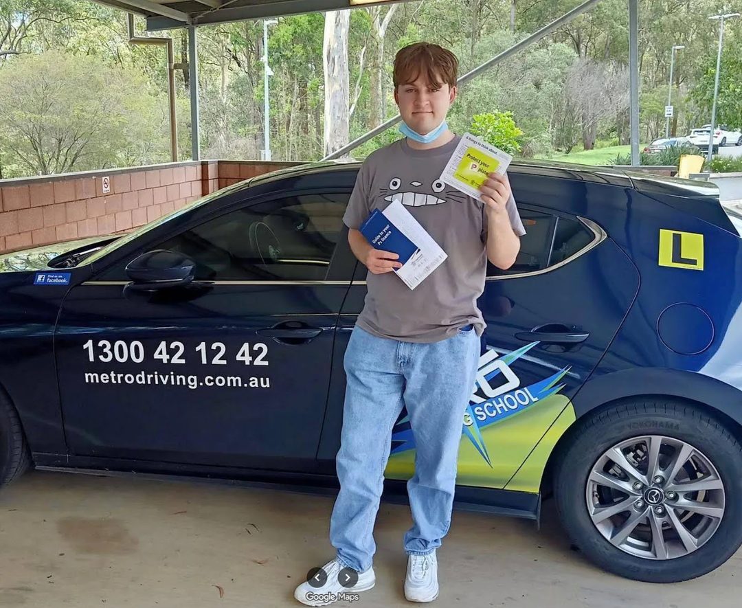 A Metro Driving School learner holding their green P-plates beside a Metro dual-control car after passing the driving test