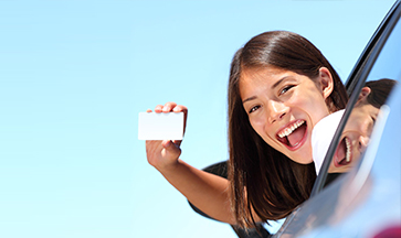 Student holding a driving licence card out of a car window