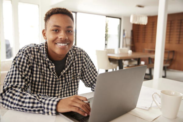 Smiling teen using a laptop at home to complete his online driver's education course