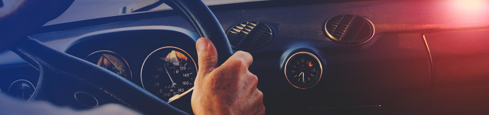 Close-up view of hands on the steering wheel and dashboard of a car.