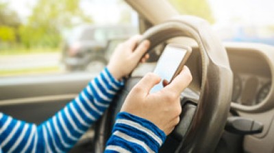 Driver holding a cell phone while behind the wheel, illustrating the dangers of distracted driving.