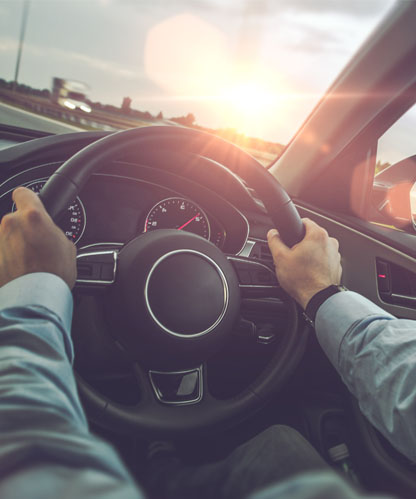 Driver's view from behind the steering wheel of an automatic car on the highway at sunset, both hands on the wheel
