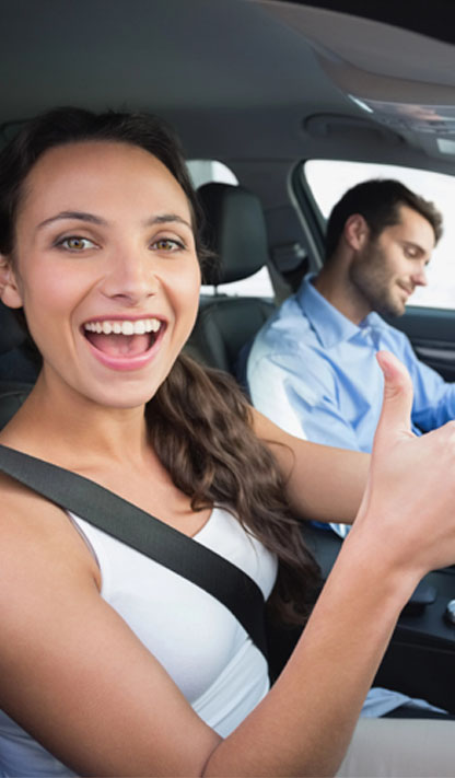Delighted learner giving a thumbs up in the driver's seat on test day while the instructor beside her completes the paperwork