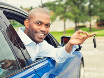 Learner smiling and holding up car keys through the open window of an automatic lesson car