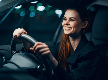 Learner driving at night with both hands on the wheel and city lights blurred behind