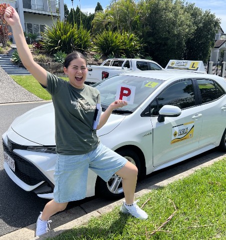 Student celebrating with a red P plate beside a Coastwide car