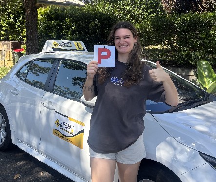Student holding a red P plate beside a Coastwide driving school car