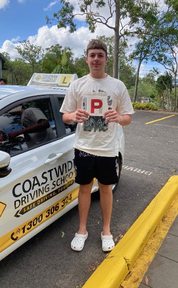 Student holding a red P plate beside a Coastwide lesson car
