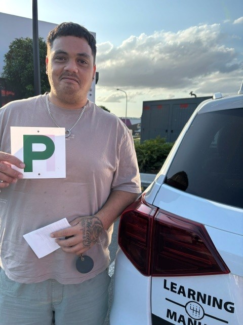 Person holding a green P plate beside a white car marked Learning Manual