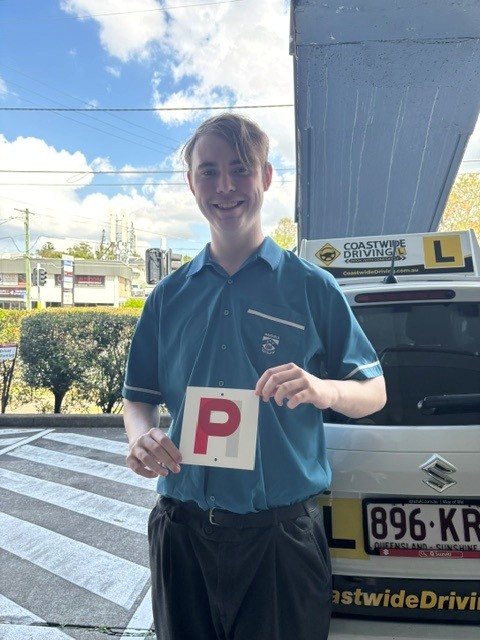 Person in a blue shirt holding a red P plate beside a Coastwide learner car