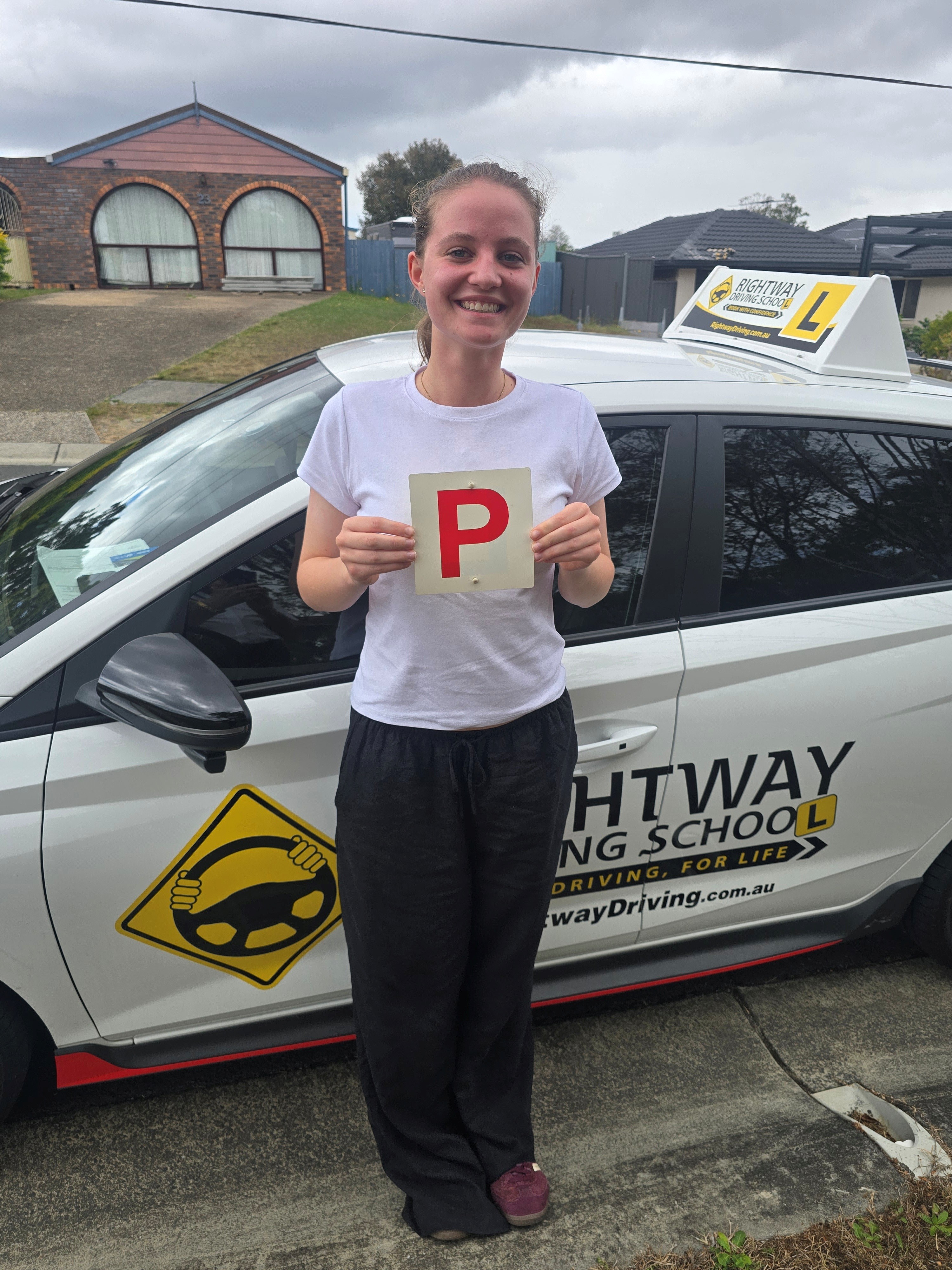 Person in a white top holding a red P plate beside a Rightway car