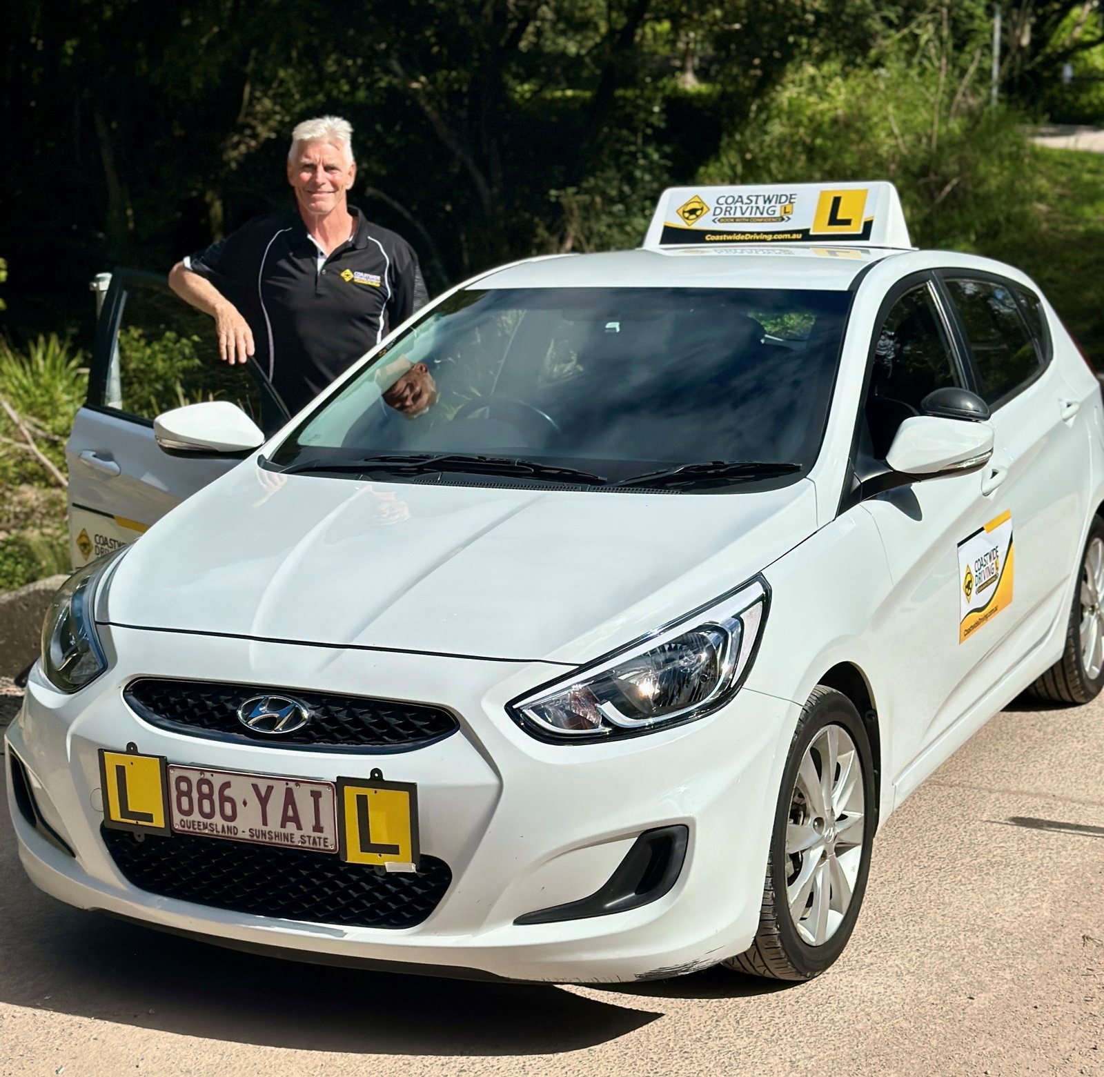 Person in a Coastwide polo beside the open door of a white learner car