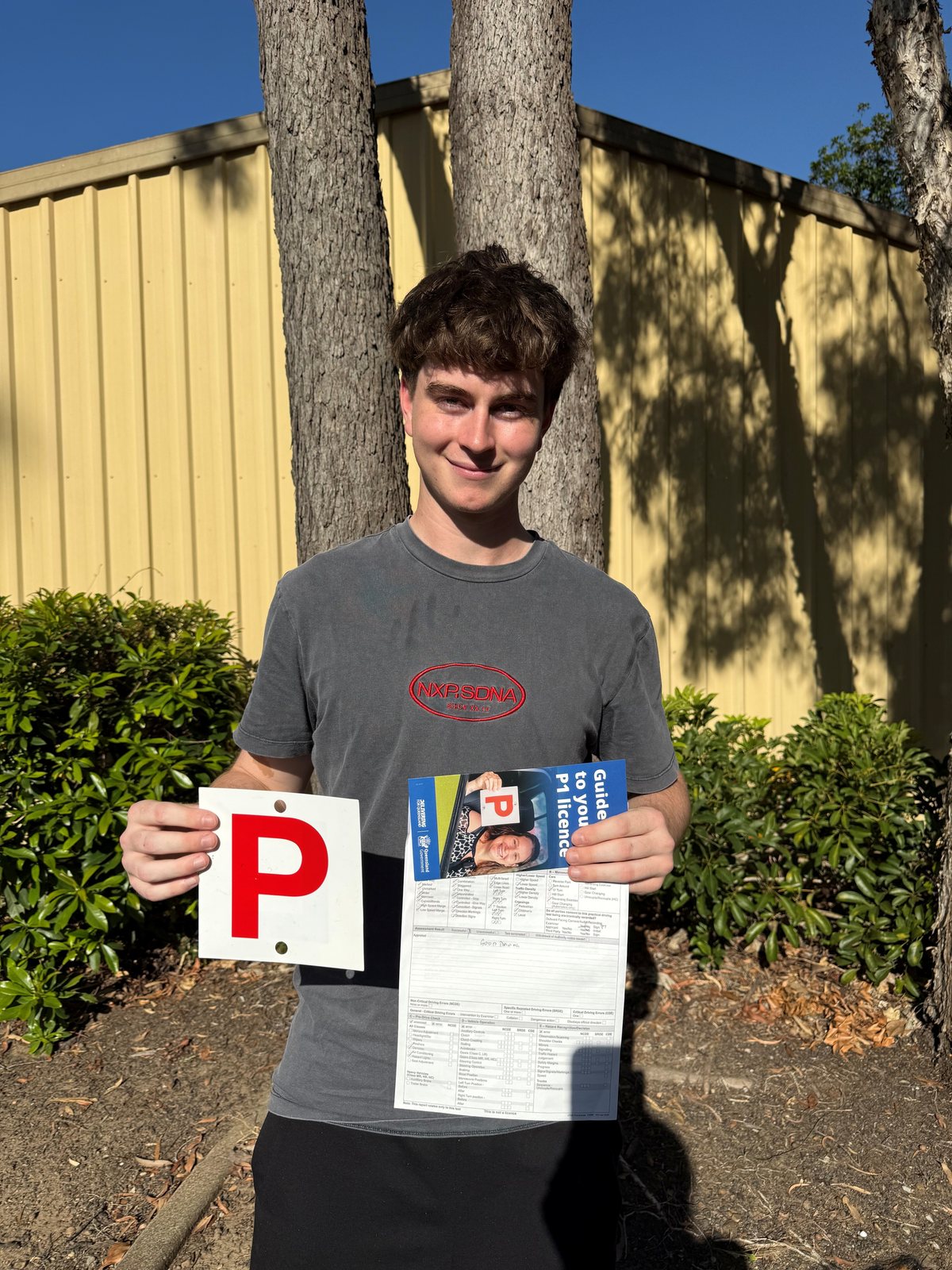 Person holding a red P plate and paperwork outdoors