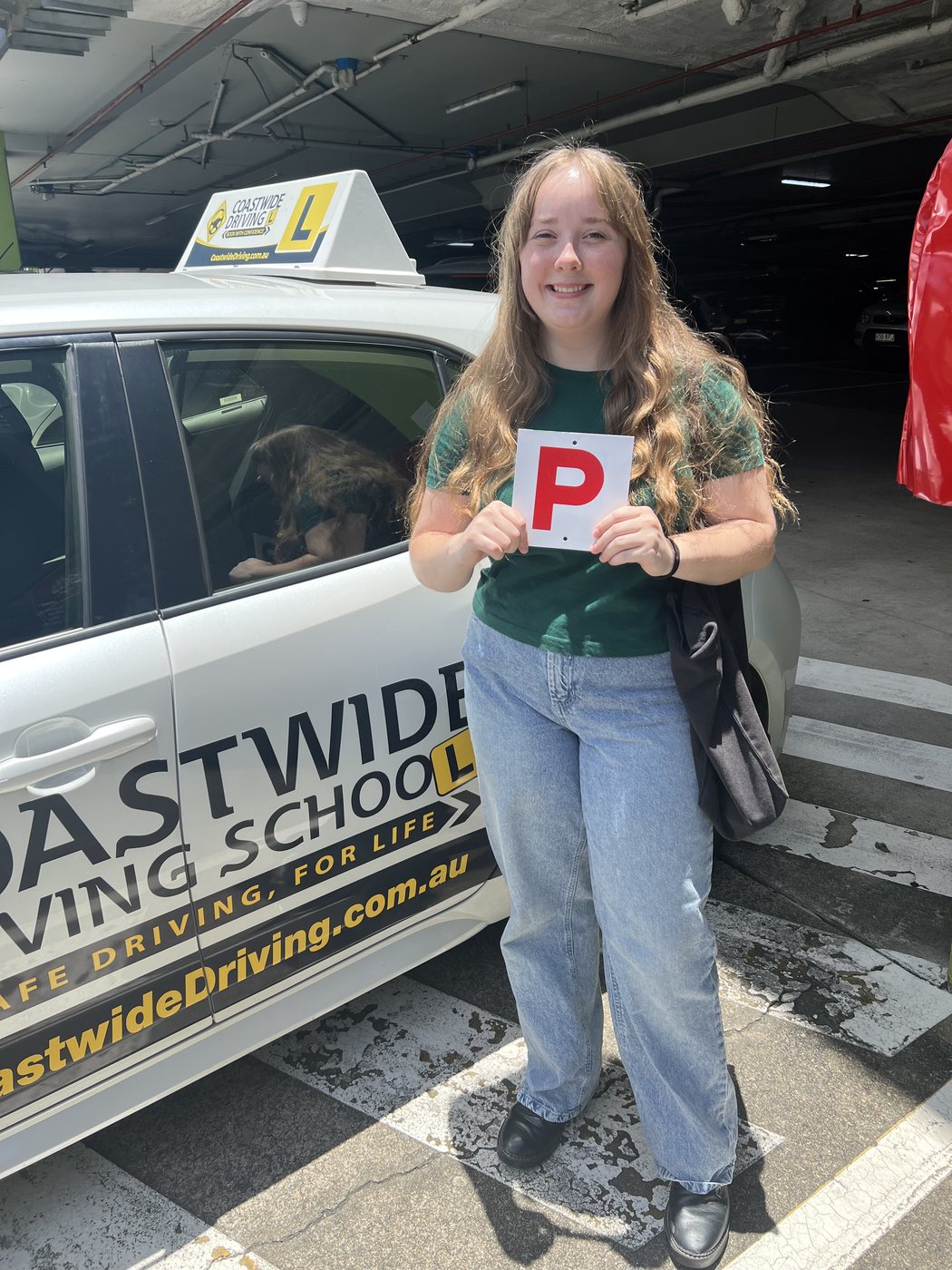 Person in a green top holding a red P plate beside a Coastwide learner car